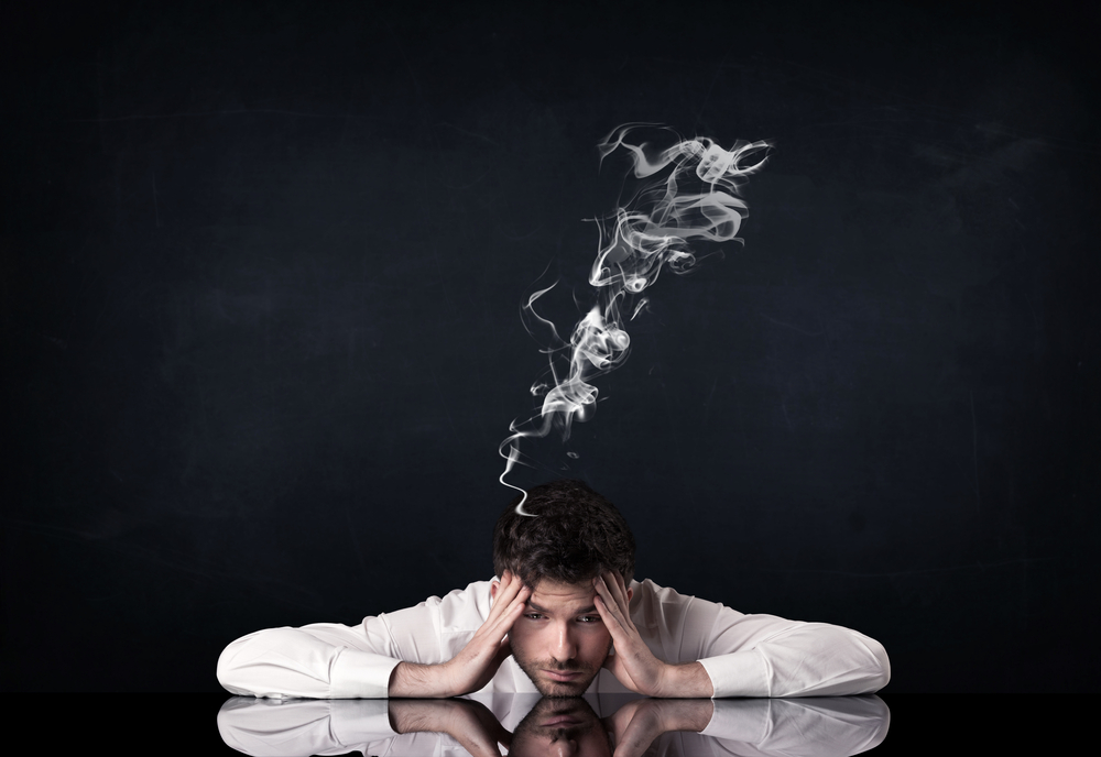 Young depressed businessman sitting with smoking head