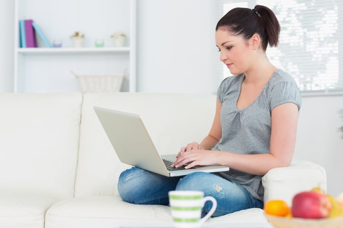 Young woman sitting on the couch in a living room and working with the laptop