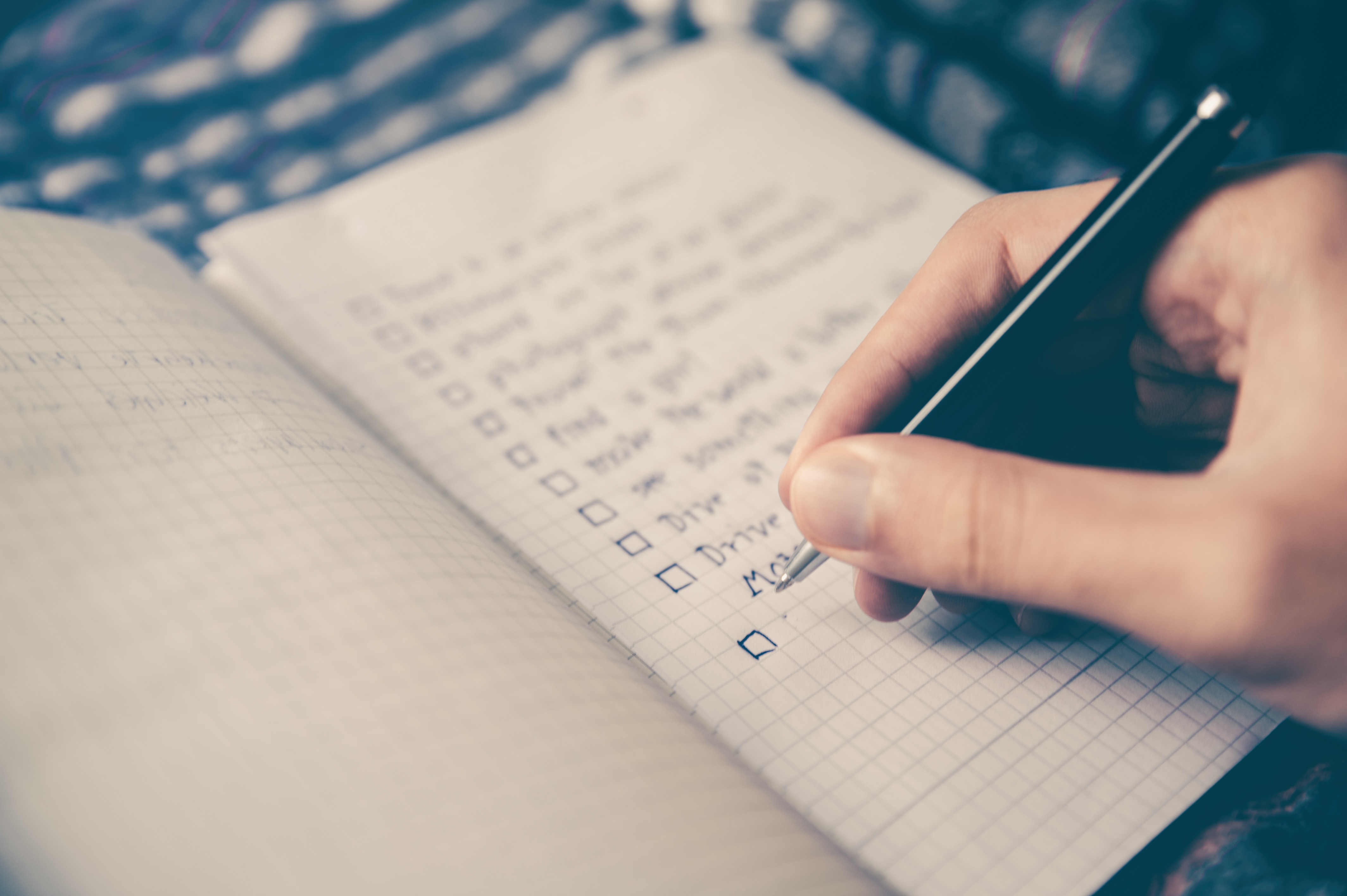 hand writing in a grid-style notebook, checking off items in a to do list for new years resolutions